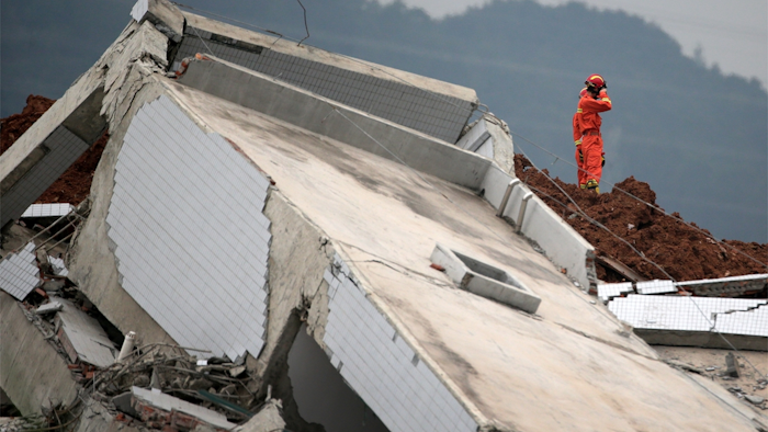A rescuer wipes his face near a damaged building as they search for potential survivors following a landslide at an industrial park in Shenzhen, in south China's Guangdong province, Tuesday, Dec. 22, 2015. A man-made mountain of excavated soil and construction waste crashed into the industrial park on Sunday, Dec. 20. (AP Photo/Andy Wong)