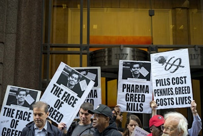 Activists hold signs containing the image of Turing Pharmaceuticals CEO Martin Shkreli.