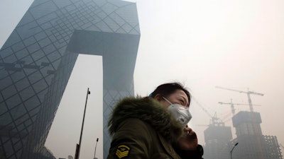 A woman wears a mask for protection against the pollution in Beijing, China, Wednesday, Dec. 9, 2015. Unhealthy smog hovered over downtown Beijing as limits on cars, factories and construction sites kept pollution from spiking even higher Wednesday, on the second of three days of restrictions triggered by the city's first red alert for smog. (AP Photo/Ng Han Guan)