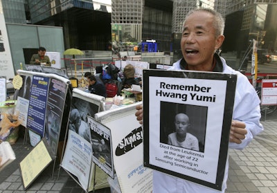 Hwang Sang-gi, a founding member of advocacy group Banolim, holds a picture of his daughter Yu-mi during an interview denouncing Samsung’s response in its latest negotiations with sick workers outside Samsung buildings in Seoul, South Korea. Yu-mi’s death from leukemia in 2007 galvanized concern about conditions at Samsung factories and South Korea’s semiconductor industry in general. (AP Photo/Ahn Young-joon)