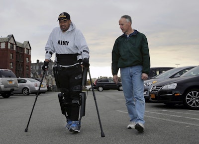 While ReWalk Robotics service engineer Tom Coulter, right, looks on, paralyzed Army veteran Gene Laureano smiles as he walks using a ReWalk device Wednesday, Dec. 16, 2015, in Bronx, N.Y. (AP Photo/Mel Evans)