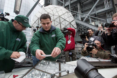 Electricians Nick Bonavita, left, and Jason Andrle install triangular crystals into a panel they are installing on the Waterford crystal ball, background, on the roof of One Times Square, Sunday, Dec. 27, 2015, in New York. Hundreds of thousands of people in Times Square are expected to watch the ball drop at midnight Thursday. (AP Photo/Mark Lennihan)