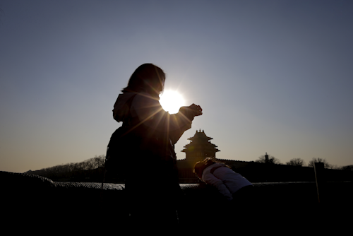 A woman is silhouetted against the sun as she walks past the Turret of the Forbidden City during a blue sky day in Beijing, Tuesday, Jan. 5, 2016. (AP Photo/Andy Wong)