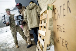 Michigan National Guard Staff Sgt. Stephen Robel, left, holds the door open while helping Flint resident Herbert Biggs, 59, as they carry cases of free bottled water to his truck as the first seven Michigan National Guard soldiers are on the ground at fire stations. (Jake May/The Flint Journal-MLive.com via AP)
