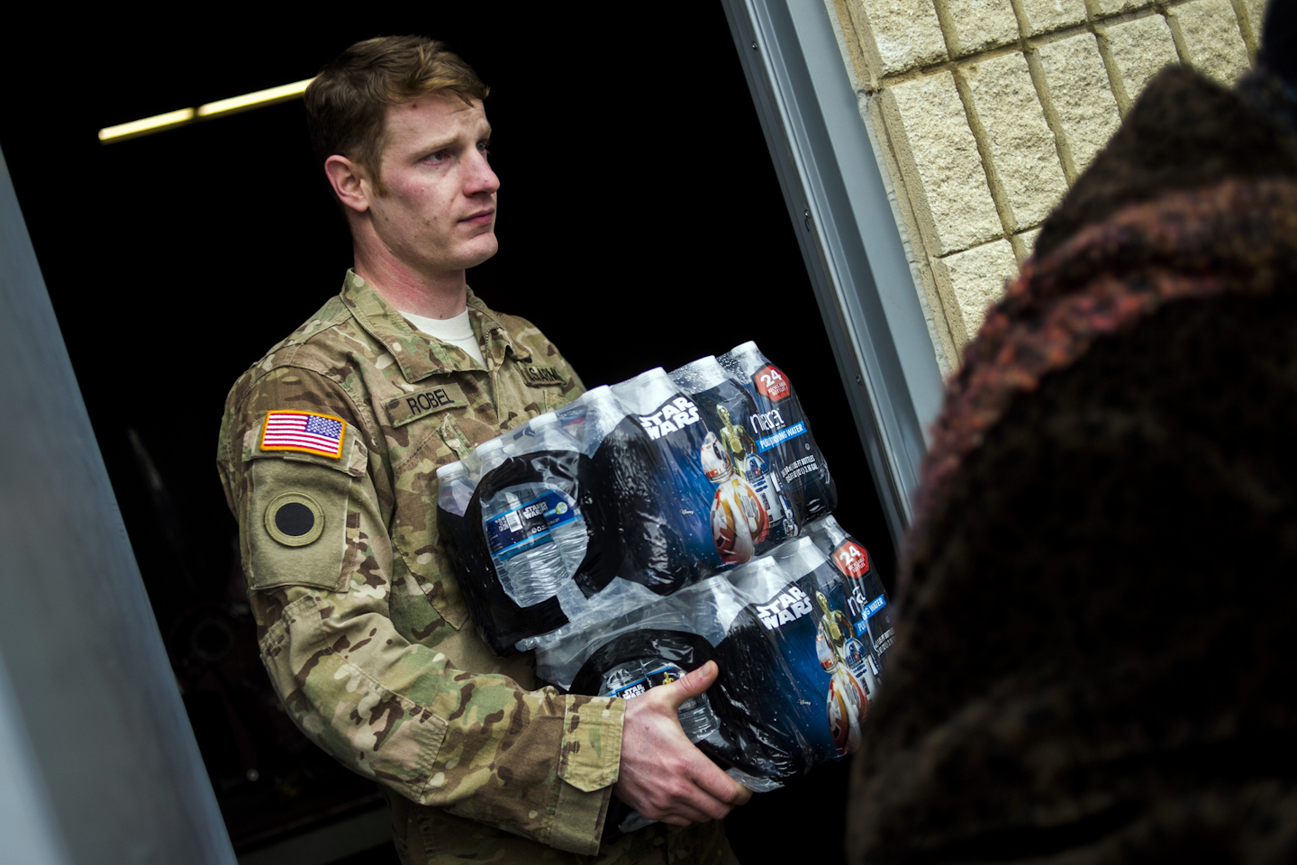 Michigan National Guard Staff Sgt. Stephen Robel helps carry a case of water to the vehicle of Flint resident Karand Houston as the first seven Michigan National Guard soldiers arrive on the ground at fire stations throughout Flint. (Jake May/The Flint Journal-MLive.com via AP)