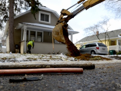 As the hole is filled in in the background, a piece of an old lead water pipe sits next to a new copper pipe at a home on Greencroft in Lansing, Mich. Lansing's municipal utility says it's nearly eliminated lead water service lines since concerns in 2004 prompted it to launch a massive program to replace them with copper lines by 2017. (Dave Wasinger/Lansing State Journal via AP)