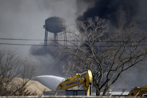 A fire officials sprays water on a large warehouse fire a day after flames engulfed the facility, Friday, Feb. 12, 2016, in Hillsborough, N.J. Firefighters have contained the massive fire and officials said the blaze didn't pose an imminent public health threat. Fire officials say plastic pellets were being stored in most of the complex, and environmental officials have been testing air quality. (AP Photo/Julio Cortez)