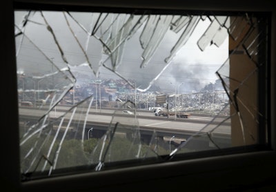 A window shattered by the shockwaves frames the site of an explosion at a warehouse in northeastern China's Tianjin municipality. (AP Photo/Ng Han Guan, File)