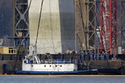 People look on as the tugboat 'Specialist' is raised out of the water under the Tappan Zee Bridge in Tarrytown, N.Y., Thursday, March 24, 2016. The tugboat that crashed and sank in the Hudson River north of New York City, killing three crew members, is being raised with a massive crane. (AP Photo/Seth Wenig)