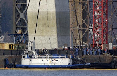 People look on as the tugboat 'Specialist' is raised out of the water under the Tappan Zee Bridge in Tarrytown, N.Y., Thursday, March 24, 2016. The tugboat that crashed and sank in the Hudson River north of New York City, killing three crew members, is being raised with a massive crane. (AP Photo/Seth Wenig)