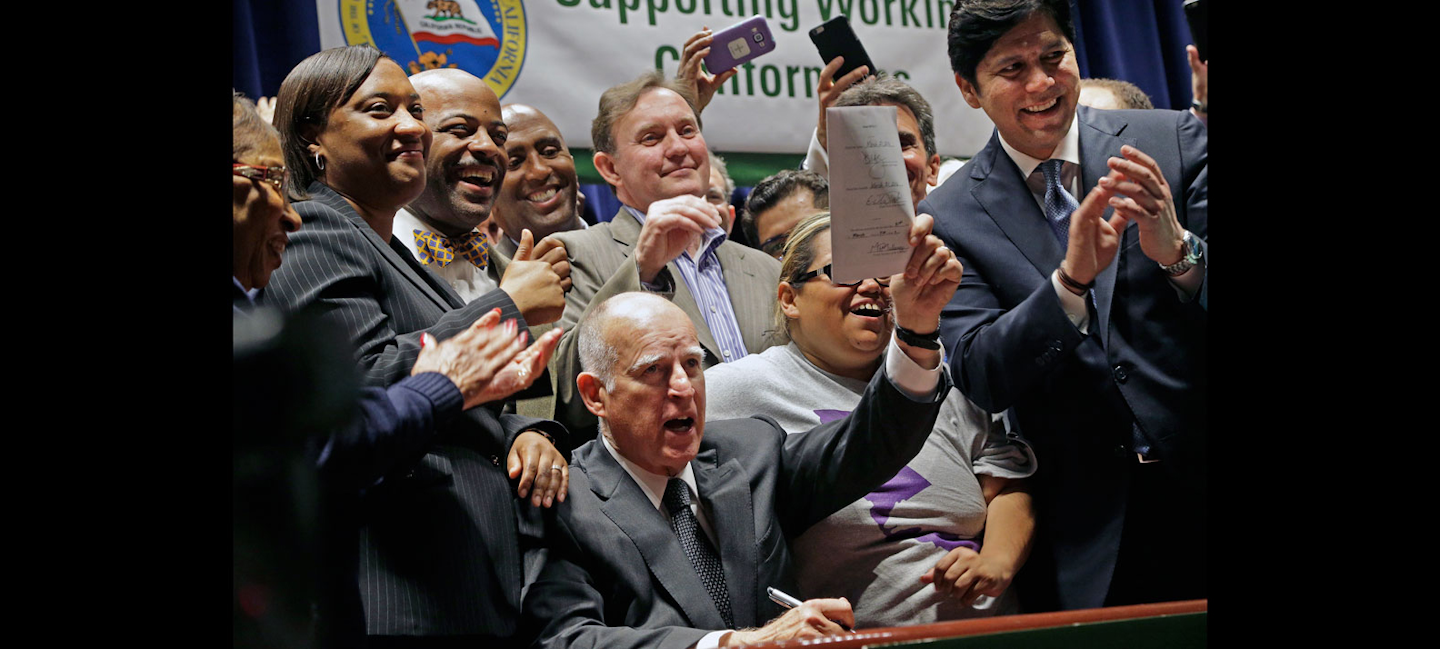 California Gov. Jerry Brown lifts a signed bill creating highest statewide minimum wage at $15 an hour by 2022 at the Ronald Reagan building in Los Angeles on Monday. (AP Photo/Nick Ut)
