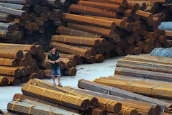 A man stands on bundles of steel pipes in a steel products dockyard along the Yangtze River in southwestern China's Chongqing Municipality. (Chinatopix via AP)