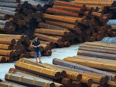 A man stands on bundles of steel pipes in a steel products dockyard along the Yangtze River in southwestern China's Chongqing Municipality. (Chinatopix via AP)