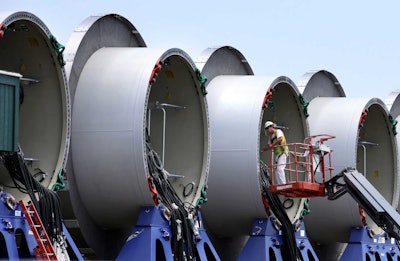 A worker stands on an elevated platform while working on partially assembled sections of wind turbine towers at a staging site for the nation's first off shore wind farm. (AP Photo/Steven Senne)