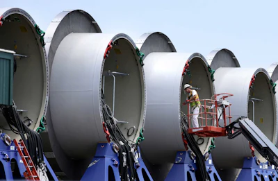 A worker stands on an elevated platform while working on partially assembled sections of wind turbine towers at a staging site for the nation's first off shore wind farm. (AP Photo/Steven Senne)