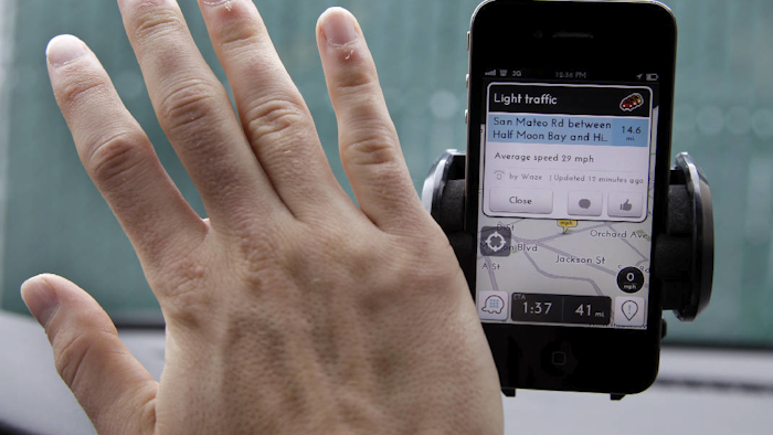 Ben Gleitzman waves his hand over a traffic and navigation app called Waze on his Apple iPhone in a Menlo Park, Calif., parking lot during a demonstration showing traffic conditions on the display. The program allows anyone using the Waze app to offer a ride to a limited pool of people trying to get to work or home. (AP Photo/Paul Sakuma, File)