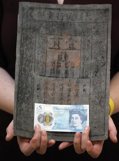 Bank of England Museum curator Jenni Adam holds the new five pound note in front of one of the World's earliest of Ming dynasty paper money at the Bank of England Museum in London. (AP Photo/Frank Augstein)