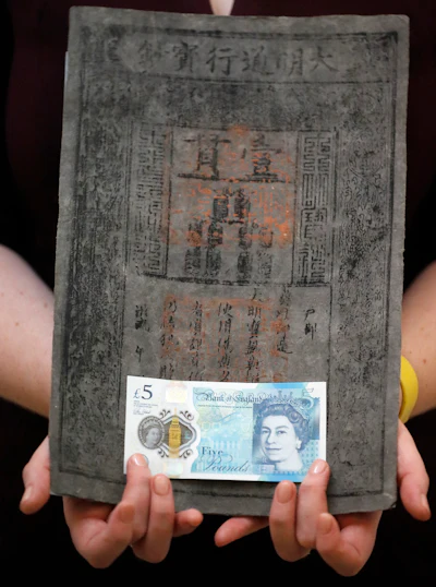 Bank of England Museum curator Jenni Adam holds the new five pound note in front of one of the World's earliest of Ming dynasty paper money at the Bank of England Museum in London. (AP Photo/Frank Augstein)