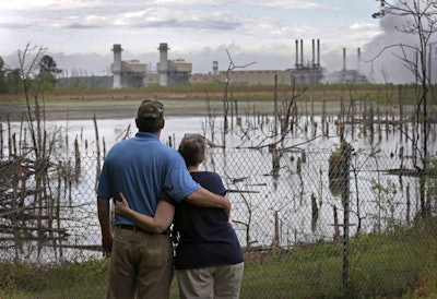Bryant Gobble, left, embraces his wife, Sherry Gobble, right, as they look from their yard across an ash pond full of dead trees toward Duke Energy's Buck Steam Station in Dukeville, N.C. (AP Photo/Chuck Burton, File)