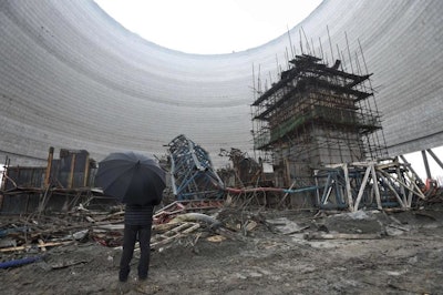 A man holding an umbrella looks at the collapsed construction site of a cooling tower for a coal-fired power plant in Fengcheng in central China's Jiangxi province. (Chinatopix via AP)