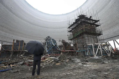 A man holding an umbrella looks at the collapsed construction site of a cooling tower for a coal-fired power plant in Fengcheng in central China's Jiangxi province. (Chinatopix via AP)