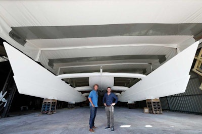 Energy Observer expedition leader Jerome Delafosse, left, and captain, Victorien Erussard, pose in front of the two floats of Energy Observer, which is the first boat to be powered solely by renewable energies and hydrogen, in Saint Malo, western France. (Pierrick Contin/Energy Observer via AP)