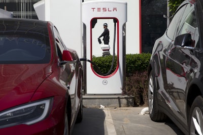 In this Friday, April 14, 2017, file photo, a security guard moves past an electric vehicle charging station in Beijing. Momentum is building worldwide for electric cars thanks to rising government fuel economy standards and climate concerns. Automakers are jumping on board. But selling those cars will be difficult unless the world builds more charging stations. (AP Photo/Ng Han Guan, File)