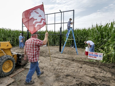 In this July 29, 2017 photo, activist Tom Genung of the organization Bold Nebraska is about to pitch a flag of the Cowboy Indian Alliance at the proposed path of the Keystone XL pipeline, in Silver Creek, Neb., where landowner Jim Carlson and activists were building solar panels. Despite new uncertainty over whether TransCanada, the builder of the Keystone XL pipeline will continue the project, longtime opponents in Nebraska aren't letting their guard down and neither are law enforcement officials who may have to react to protests if it wins approval. (AP Photo/Nati Harnik)