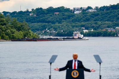 A coal barge is positioned as a backdrop behind President Donald Trump as he speaks during a rally at the Rivertowne Marina in Cincinnati. President Donald Trump personally promised to activate emergency legal authorities to keep dirty or economically uncompetitive coal plants from shutting down, a top American coal company said. The Trump administration now says it has no plans to do so. (AP Photo/John Minchillo, File)