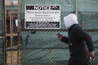 In this Dec. 11, 2017 photo, a man walks past a notice for the Martin Aaron Inc. Superfund site in Camden, N.J. Nearly 2 million people in the U.S. who live within a mile of 327 Superfund sites in areas prone to flooding or vulnerable to rising seas caused by climate change, according to an Associated Press analysis of flood zone maps, census data and U.S. Environmental Protection Agency records. (AP Photo/Matt Rourke)