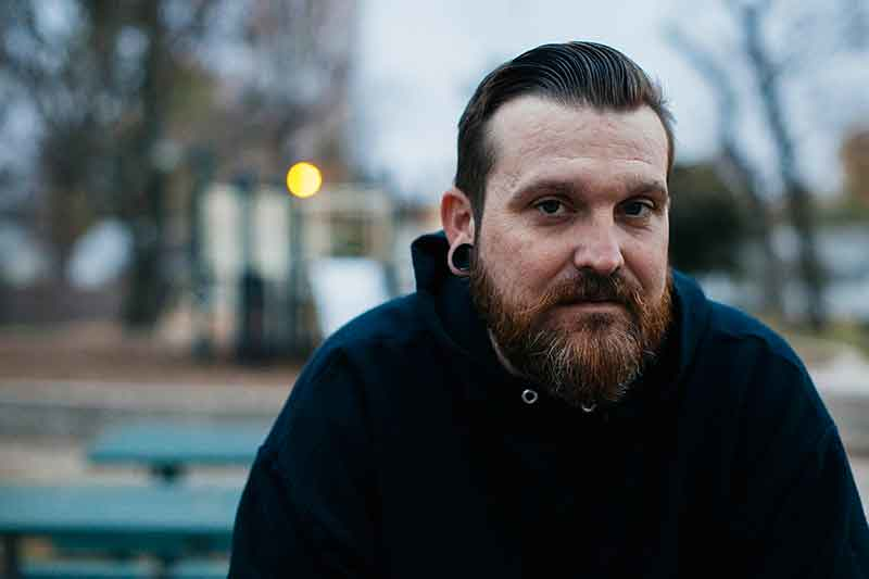 In this Nov. 29, 2017 photo provided by Reveal from The Center Investigative Reporting, Dustin Barnes sits in a park near his home in Tulsa, Okla. Retired Oklahoma judge Thomas Landrith started his own rehab work camp called SOAR, Southern Oklahoma Addiction Recovery, where defendants must work full-time for free at a Coca-Cola bottling plant and other companies, under threat of prison. Barnes was sent to SOAR in 2015 and called the people who run it “crooks.” (Shane Bevel/Reveal via AP)