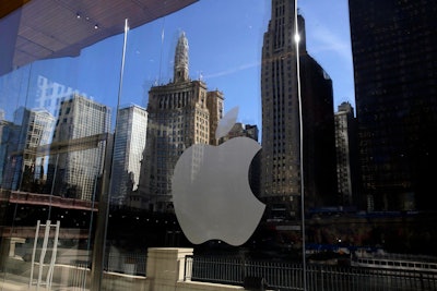 Buildings and a tour boat are reflected on the mirror behind an Apple logo during a preview event at a new Apple Michigan Avenue store, in downtown Chicago. On Wednesday, Jan. 17, 2018, Apple announced it is planning to build another corporate campus and hire 20,000 workers during the next five years as part of a $350 billion commitment to the U.S. economy. (AP Photo/Kiichiro Sato, File)