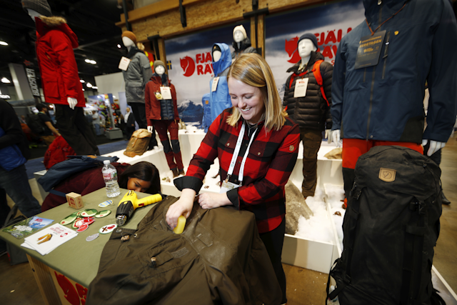 Aundrea Dawkins of Louisville, Colo., puts a protective wax on a Fjallraven coat in the Swedish company's booth at the Outdoor Retailer and Snow Show in the Colorado Convention Center Friday, Jan. 26, 2018, in Denver. Sales of outdoor equipment are slipping as millennials drive changes in U.S. consumer habits by favoring clothes and sporting goods that are less specialized and more versatile, analysts say. (AP Photo/David Zalubowski)