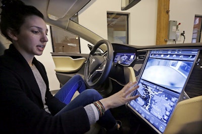 In this Feb. 4, 2015, file photo, Tesla product specialist Kat Brand explains the control panel on the electric car at a dealership for the vehicle in Seattle. Image credit: AP Photo/Elaine Thompson, File