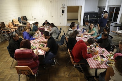 In this Oct. 10, 2017 file photo, a group of homeless people, including Ellen Tara James-Penney (wearing blue) left, a lecturer at San Jose State University, receive a meal at Grace Baptist Church in San Jose, Calif. Image credit: AP Photo/Marcio Jose Sanchez, File