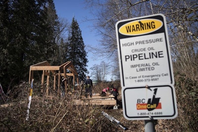 A sign warns of an underground pipeline as people construct a 'watch house' near a gate leading to Kinder Morgan's property during a protest against the company's Trans Mountain pipeline expansion in Burnaby, British Columbia, Saturday, March 10, 2018. (Darryl Dyck/The Canadian Press via AP)