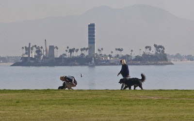In this Jan. 14, 2015, file photo, people walk on the waterfront in Long Beach, Calif., past a man-made island built to pump oil just off shore. Oil and gas companies drilling off the coast of Southern California violated state regulations nearly 400 times in the past three years, according to a report by an environmental group. (AP Photo/Damian Dovarganes)