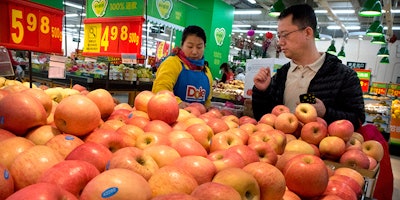 FILE - In this March 23, 2018, file photo, a woman wearing a uniform with the logo of an American produce company helps a customer shop for apples a supermarket in Beijing. China raised import duties on a $3 billion list of U.S. pork, fruit and other products Monday, April 2, 2018 in an escalating tariff dispute with President Donald Trump that companies worry might depress global commerce. (AP Photo/Mark Schiefelbein, FILE)