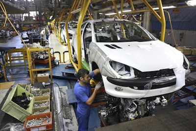 In this Oct. 11, 2014 file photo, an Iranian worker assembles a Peugeot 206 at the state-run Iran-Khodro automobile manufacturing plant near Tehran, Iran. Image credit: AP Photo/Ebrahim Noroozi, File