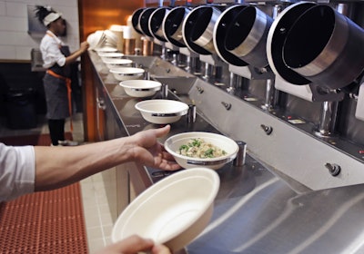 A worker lifts a lunch bowl off the production line at Spyce, a restaurant which uses a robotic cooking process, in Boston, Thursday, May 3, 2018. Robots can't yet bake a souffle or fold a burrito, but the new restaurant in Boston is employing what it calls a 'never-before-seen robotic kitchen' to cook up ingredients and spout them into a bowl. (AP Photo/Charles Krupa)