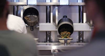 Customers wait as their automatically prepared food is dropped from a cooking pot into a bowl at Spyce, a restaurant which uses a robotic cooking process in Boston, Thursday, May 3, 2018. Robots can't yet bake a souffle or fold a burrito, but the new restaurant in Boston is employing what it calls a 'never-before-seen robotic kitchen' to cook up ingredients and spout them into a bowl. (AP Photo/Charles Krupa)