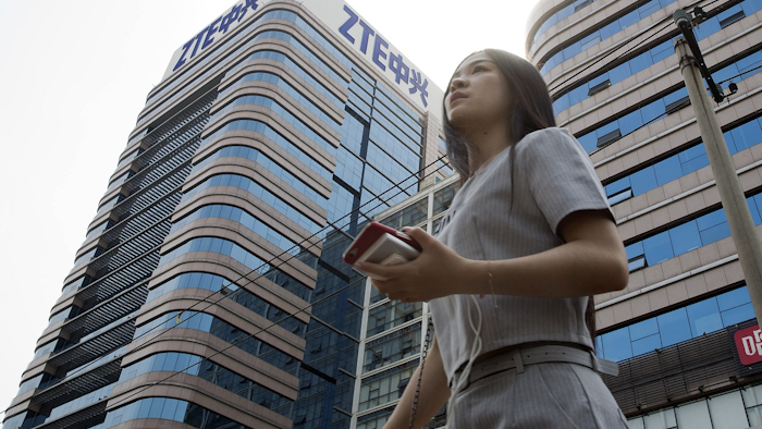 In this May 8, 2018, file photo, a woman passes by a ZTE building in Beijing, China. Image credit: AP Photo/Ng Han Guan, File