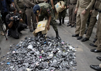 A Thai law-enforcement officer unloads a box full of mobile batteries during a raid at a factory accused of importing and processing electronic waste in the suburbs of Bangkok, Thailand on Thursday, June 21, 2018. Image credit:AP Photo/Gemunu Amarasinghe