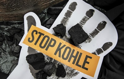 Coal lay on a poster with slogan 'Stop Coal', during demonstration demanding the end of burning coal to produce electricity, in Berlin, Germany, Sunday, June 24, 2018. Image credit: Paul Zinken/dpa via AP