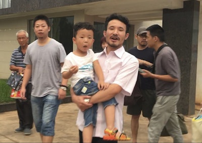 In this June 28, 2017 file image taken from video, Chinese labor activists Hua Haifeng, center, carries his son Bo Bo, and Li Zhao, second left, leave a police station after being released in Ganzhou in southern China's Jiangxi Province. Image credit: AP Photo/Gerry Shih, File