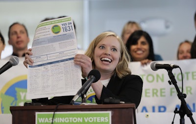 In this May 10, 2018, file photo, Abigail Doerr, campaign director for Yes on 1631, holds up an initiative petition with signatures on it, at a rally to kick off the campaign for 'Yes on 1631,' in Seattle Washington. Image credit: AP Photo/Ted S. Warren, File