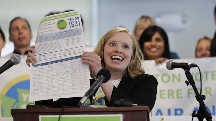 In this May 10, 2018, file photo, Abigail Doerr, campaign director for Yes on 1631, holds up an initiative petition with signatures on it, at a rally to kick off the campaign for 'Yes on 1631,' in Seattle Washington. Image credit: AP Photo/Ted S. Warren, File