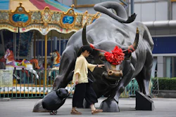 A woman pulls a 2 wheel trolley loaded with goods touches a bull statue on display outside a retail and wholesale clothing mall in Beijing, Monday, July 9, 2018. Image credit: AP Photo/Andy Wong