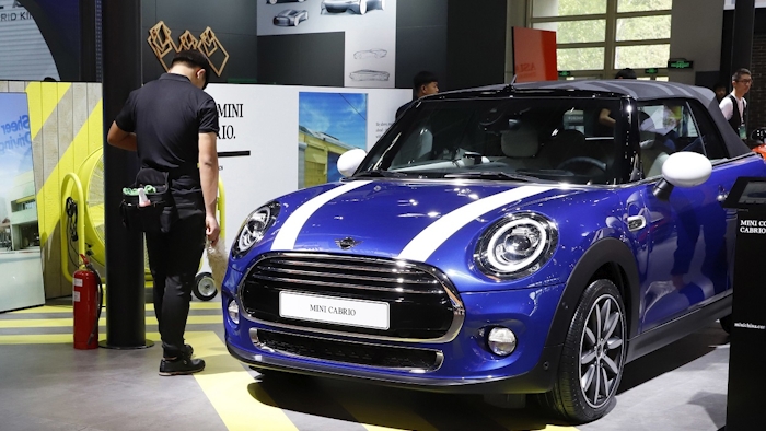 In this April 26, 2018, photo, a security guard stands near MINI cars displayed at the China Auto Show in Beijing. Image credit: (AP Photo/Ng Han Guan