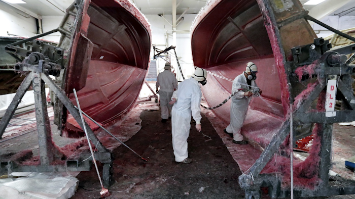Workers apply fiberglass to the resin frame of a boat at Regal Marine Industries in Orlando, Fla., Wednesday, July 11, 2018. Image credit: AP Photo/John Raoux